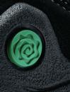 Preview: Das Bild zeigt einen schwarzen Schuh mit einem runden, grünen Detail in Form einer aufgerollten Rose. Die Oberfläche wirkt strukturiert und leicht rau.