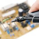 Preview: In the picture, you can see a hand holding a pair of pliers that is gripping a resistor. In the background, a circuit board with various electronic components can be seen out of focus.