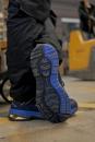 Preview: The image shows the underside of a blue shoe on a floor. The sole features a distinctive, non-slip tread with various patterns and lines that provide good traction.
