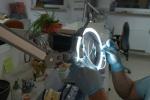 Preview: A person with blue gloves is working with a tool under a magnifying lamp. The workspace is neat and contains various tools and materials.