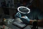 Preview: A person is wearing gloves and working under a magnifying lamp. In front of them lies a processed model. The room is dimly lit to enable precise work.