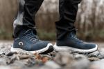 Preview: Das Bild zeigt zwei Füße in blauen, robusten Schuhen, die auf einem kieselsteinhaltigen Boden stehen. Der Untergrund ist uneben, umgeben von unscharfem, natürlichem Hintergrund.