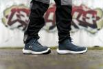 Preview: Das Bild zeigt Füße, die in sportlichen, dunkelblauen Schuhen stecken. Die Person trägt schwarze, bequeme Hosen. Im Hintergrund ist bunte Graffiti-Kunst auf einer Wand zu sehen.