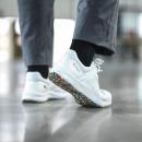 Preview: Das Bild zeigt einen Fuß in einem weißen Sneaker mit buntem, strukturiertem Sohlenrand. Der Träger trägt graue Hosen und schwarze Socken. Die Umgebung wirkt modern und hell.