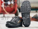 Preview: The image shows a pair of safety shoes with a sturdy, textured sole. The shoes are black with orange accents and a practical closure system.