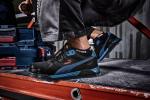 Preview: The image shows a foot in a black PUMA safety shoe with blue accents, standing on a red work surface. Toolboxes are visible in the background.