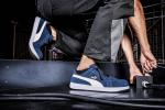 Preview: The image shows a part of a body in athletic clothing, striking a dynamic pose on a dark background. The shoes are dark blue with white accents.