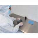 Preview: A person in protective clothing is sitting at a table. They are holding an object in their hand and working with it. There is a blue cloth and a bottle on the table.