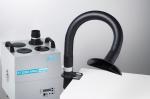 Preview: The image shows a smoke extraction device. It has a large, gray body with several openings on top. A flexible hose leads to an open, black exit area.