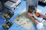 Preview: In the picture, you can see a work desk with technical equipment. A person is holding a screwdriver and working on an open case to repair electronic components. Around them, screws and tools are scattered.
