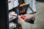 Preview: A person is holding a screwdriver and working on an electrical panel, which is equipped with multiple devices and colorful cables.