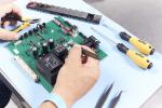 Preview: In the image, you can see a manual assembly or repair of a green circuit board with many electronic components. Next to it, there are screwdrivers and pliers.