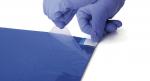 Preview: In the picture, you see a hand with blue gloves peeling a transparent film from a blue sheet. The surface is smooth and shiny.