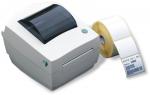 Preview: The image shows a white label printer with a glossy lid and a green button. Next to it is a roll of white labels that is being unrolled.
