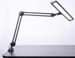 Preview: Das Bild zeigt eine schwarze Tischlampe mit einem flexiblen Armsystem. Der Lampenkopf ist länglich und hat eine helle Lichtquelle, die schräg nach unten gerichtet ist.