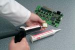 Preview: One hand is holding a circuit board with various components. In the other hand, a nozzle is being used to apply some glue. Additionally, there is a tube of glue on the surface.